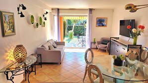 Een moderne woonkamer met een bank, een glazen eettafel en een televisie. Er is een balkon met uitzicht op groen.