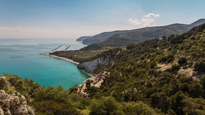 Eine Küstenlandschaft mit freiem Blick auf das Meer, eine kurvenreiche Straße durch die Hügel und eine Klippe mit Vegetation.