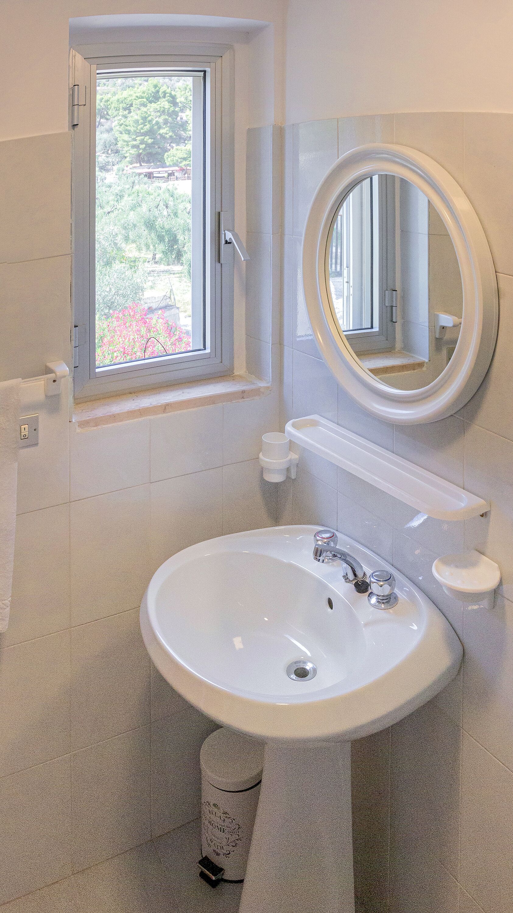 Ein Badezimmer mit einem weißen Waschbecken, einem Fenster und einem Spiegel.