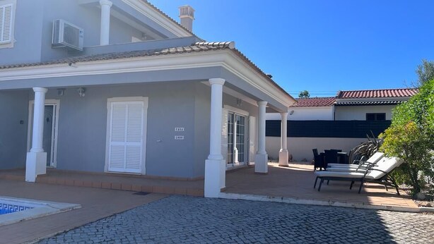 Una casa de dos pisos con un patio cubierto, una piscina y un jardín pequeño.