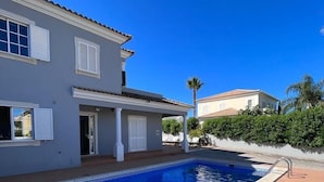 Una propiedad residencial con piscina, un patio cubierto y una casa de dos pisos con techo de tejas.