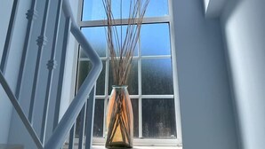 Una habitación con un ventanal grande, una barandilla blanca y un jarrón con ramas.