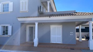 Una casa de dos pisos con piscina, contraventanas blancas y techo de tejas.