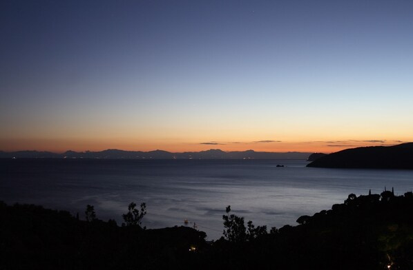 A coastal landscape at dusk with a calm sea, distant mountains, and a clear sky. - ELBA ISLAND SPLENDID VILLA WITH PANORAMA, TERRACE, WIFI AND AIR CONDITIONING (Capoliveri)