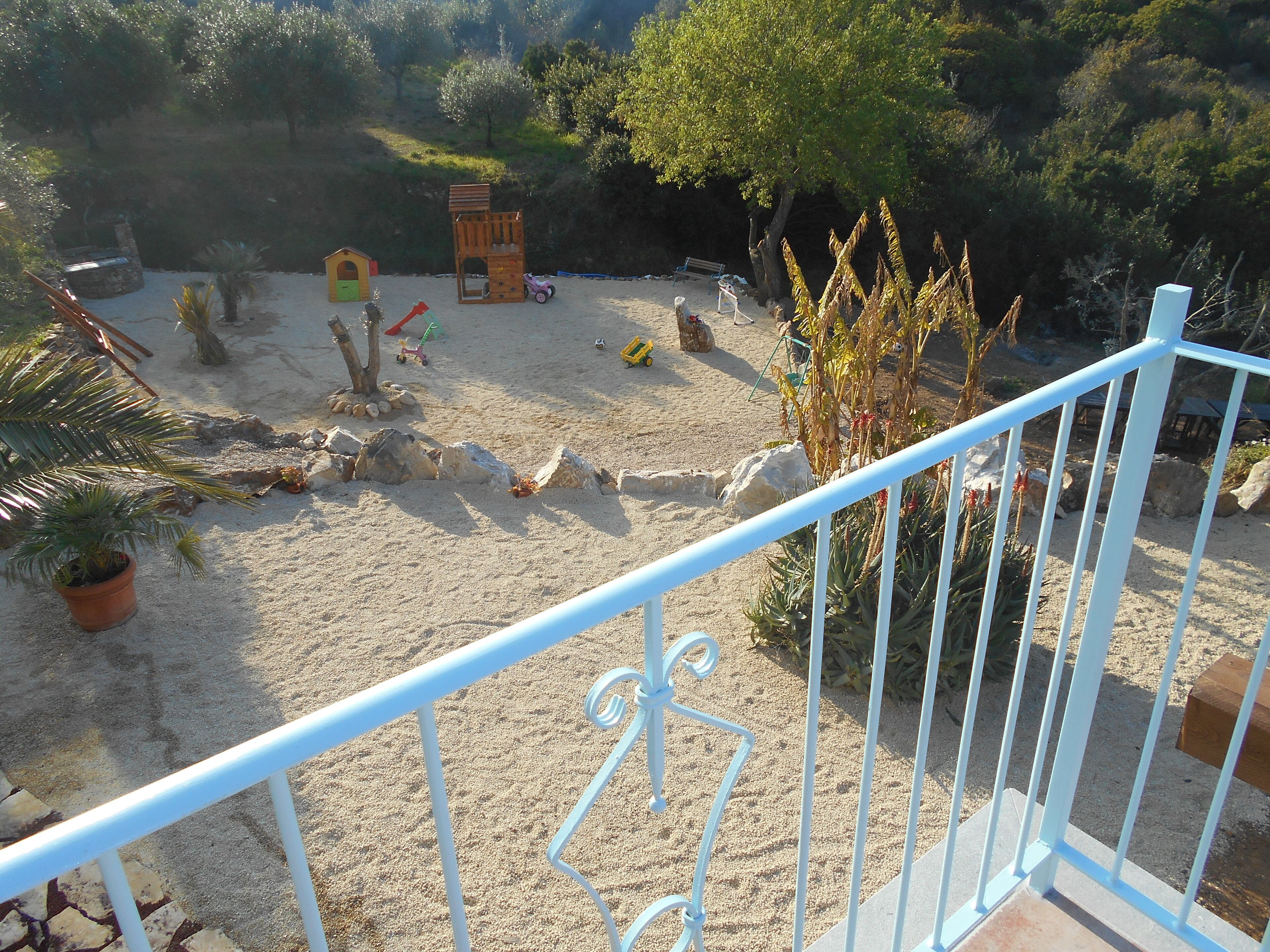 Ein Sandspielplatz im Freien mit einem hölzernen Spielhäuschen, einer kleinen Rutsche und verschiedenen Spielsachen.