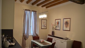 A compact kitchen with a dining table, chairs, and a small island. There are framed artworks on the wall and a chandelier above the island.