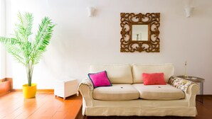 A living room with a beige sofa, two cushions, a potted plant, a mirror, and a small table with a lamp. - Apartment 3 minutes from the Spanish Steps (2 rooms) with a / c  (Roma)