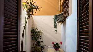 A narrow hallway with a potted plant, a hanging plant, and a small table with flowers. - Apartment 3 minutes from the Spanish Steps (2 rooms) with a / c  (Roma)