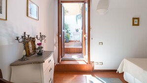 A room with a bed, a dresser, a candelabra, and a door leading to an outdoor area with a table and chairs. - Apartment 3 minutes from the Spanish Steps (2 rooms) with a / c  (Roma)