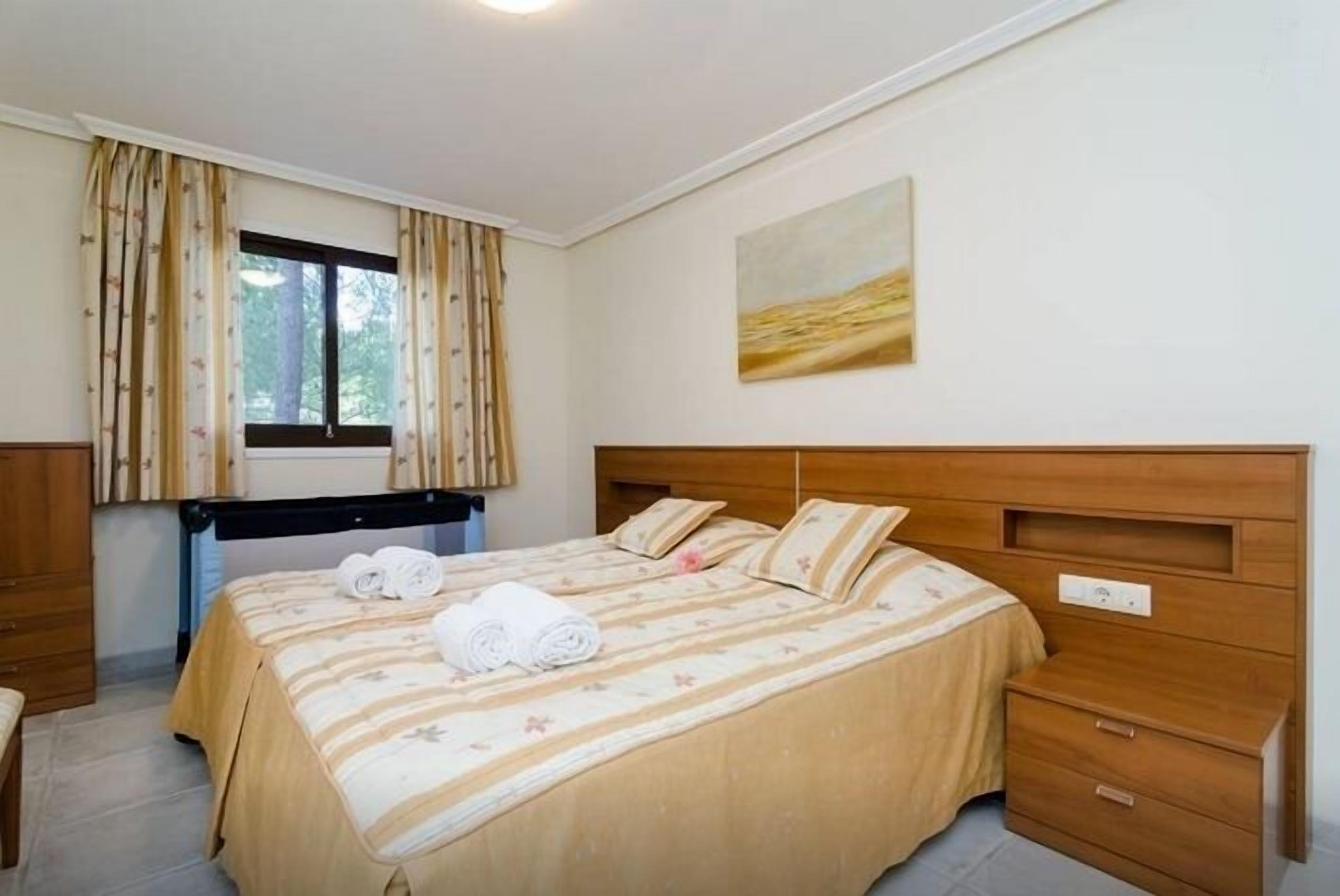 A bedroom with a bed, a nightstand, a window with curtains, and a painting on the wall.