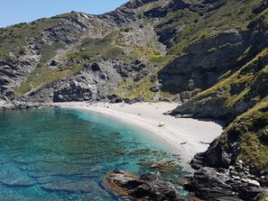 Un paysage côtier caractérisé par des eaux turquoise limpides, des falaises rocheuses et une plage de sable.