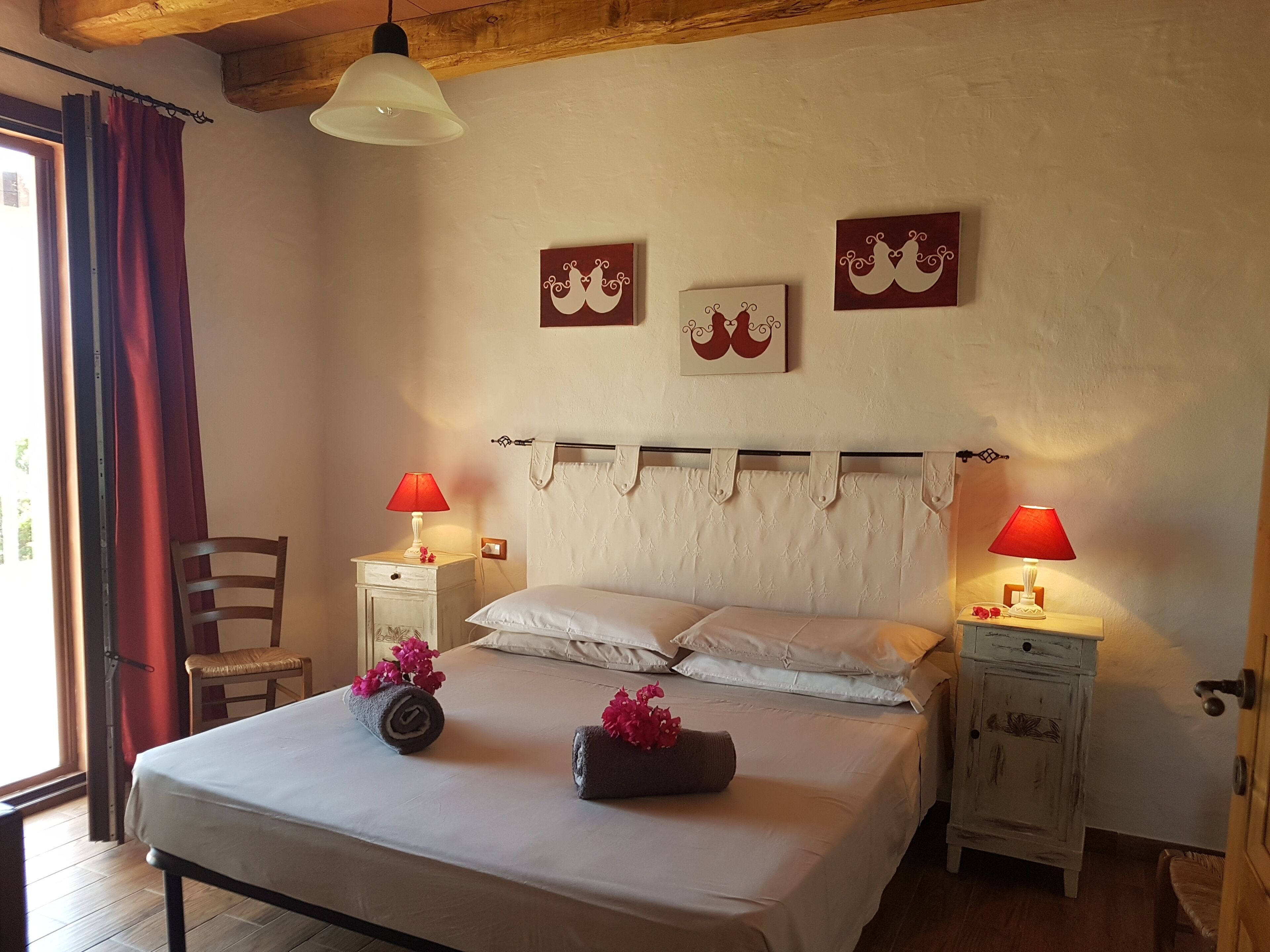 Un dormitorio con una cama, dos mesitas de noche con lámparas, una silla y una ventana con cortinas.