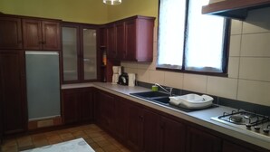 Une cuisine avec des meubles de rangement en bois, un réfrigérateur, un évier, une cuisinière et une fenêtre avec des rideaux.