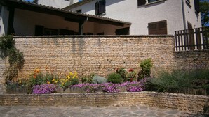 Un mur de pierre avec un jardin devant un bâtiment doté d’un toit en pente et de volets en bois.