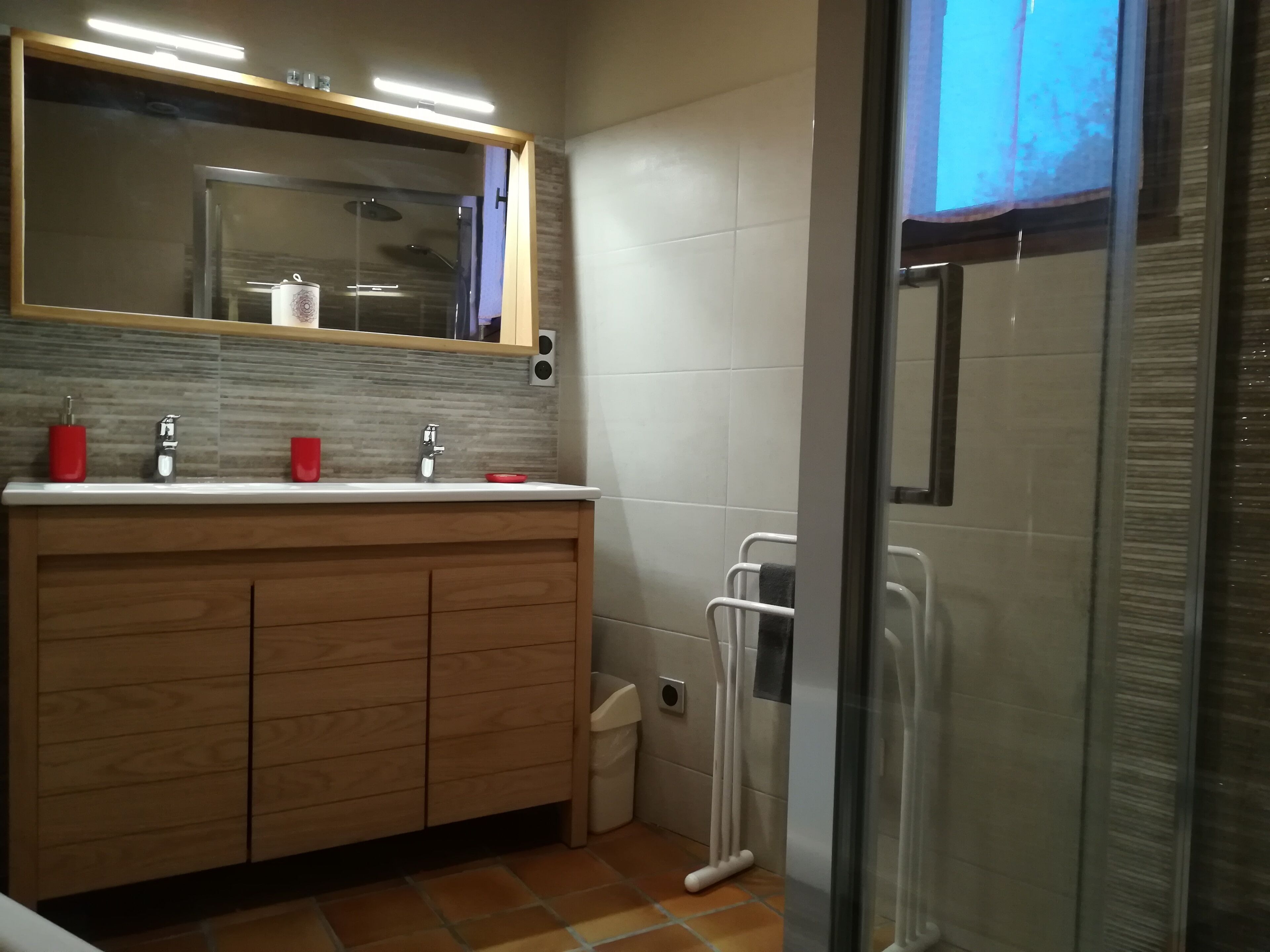 A modern bathroom with a wooden vanity, a glass shower enclosure, and a tiled floor.