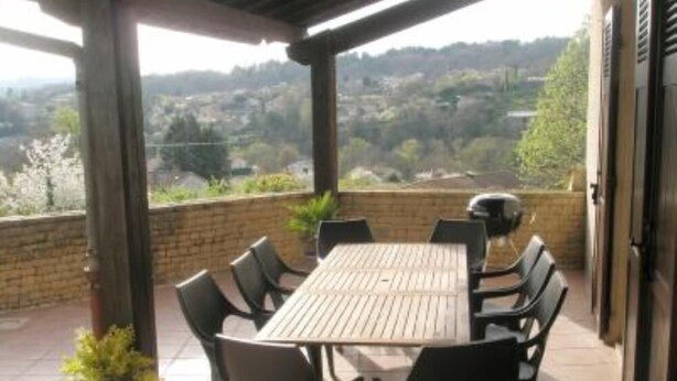 Une terrasse couverte avec une table et des chaises, un barbecue et une vue sur un paysage vallonné.