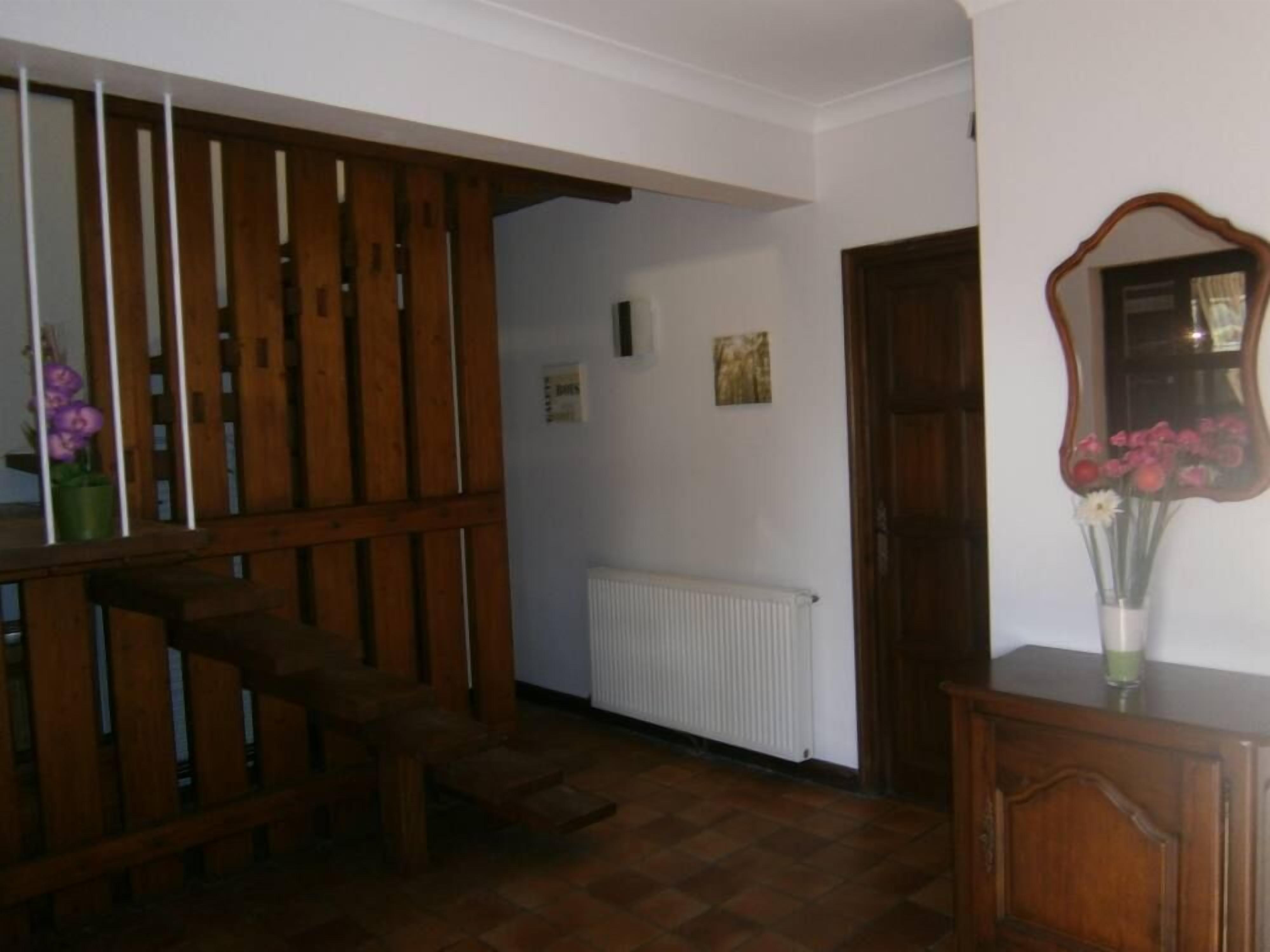A room with a wooden staircase, a radiator, a wooden door, and a mirror with flowers.