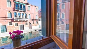 Vista por la ventana de un canal con edificios, un marco de madera y una maceta.