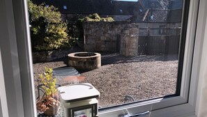 Vista desde una ventana a un patio con un pozo de piedra, suelo de grava y una pared de piedra.
