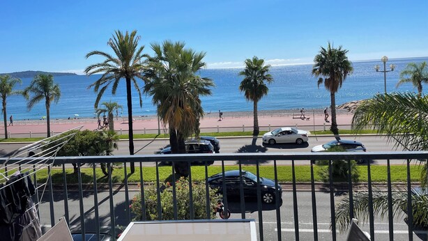 A balcony with a view of the beach, palm trees, and parked cars. - Stunning 2 bed waterfront apartment on Nice Promenade beside the Radisson Hotel (Nice)