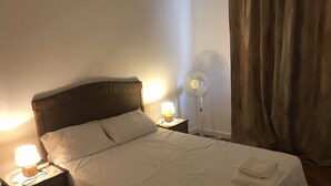 A neatly made bed with white linens, two bedside lamps, and a standing fan. - Stunning 2 bed waterfront apartment on Nice Promenade beside the Radisson Hotel (Nice)