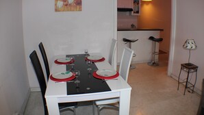 A dining area with a white table set for four, including plates, glasses, and cutlery. There are two chairs on each side of the table. A small table with a lamp is visible in the corner. - Stunning 2 bed waterfront apartment on Nice Promenade beside the Radisson Hotel (Nice)