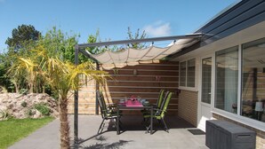 Un patio con mesa y sillas, una palmera y un área techada con vista a la casa.