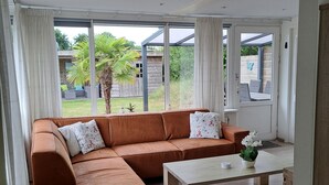 Una sala de estar moderna con un sofá modular, una mesa de centro de madera y ventanas amplias que dan a un paisaje exterior.