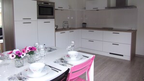 Una cocina moderna con armarios blancos, horno empotrado y microondas. Hay una mesa de comedor preparada con platos, vasos y un jarrón de flores.