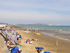 A beach with people relaxing, a pier, and cliffs in the background. - Lovely Bright Garden Apartment overlooking RSPB reserve. Brading (Brading Isle of Wight)