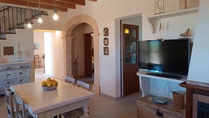 A spacious living area with a wooden staircase, a dining table with fruit, a television, and a fireplace.