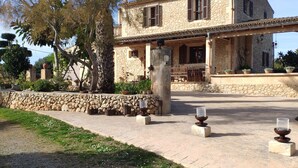 A stone house with a covered porch, outdoor seating, and a large tree in the yard.