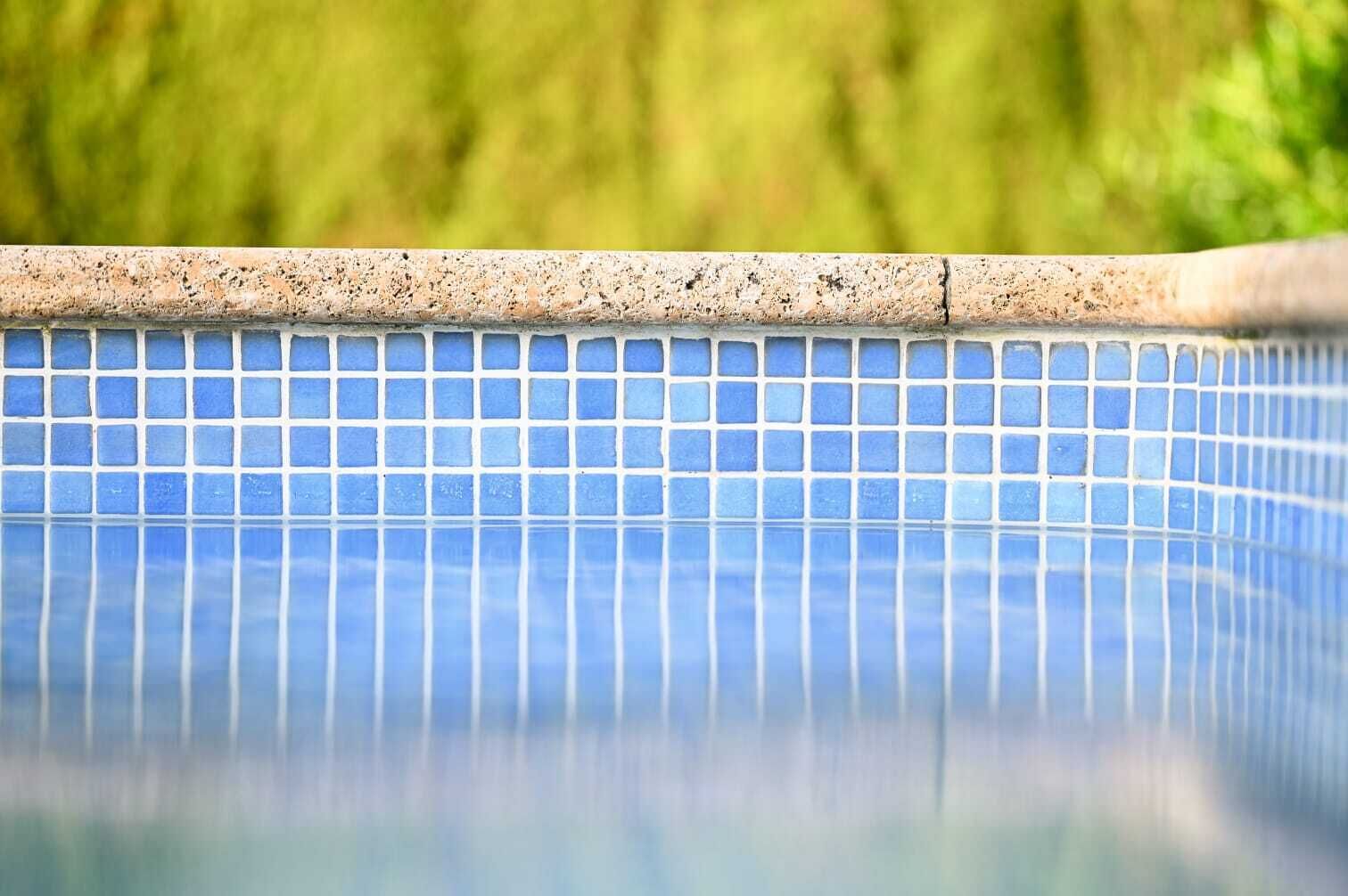 A clear view of a swimming pool with blue tiles and a stone border.