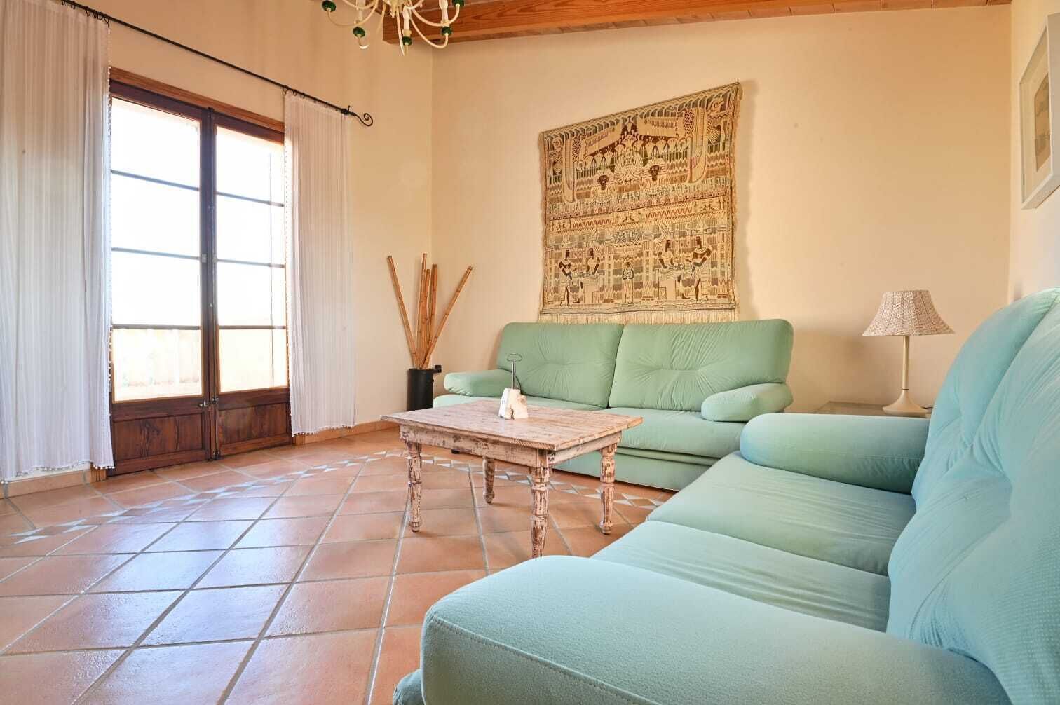 Un salon avec un canapé vert, une table basse en bois et une grande tapisserie murale.