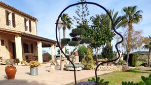 A stone building with a patio area, surrounded by various plants and a large rock in the foreground.