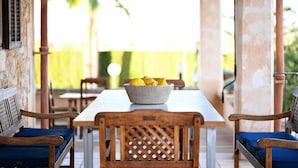 A covered outdoor dining area with a table, chairs, and a bowl of lemons.
