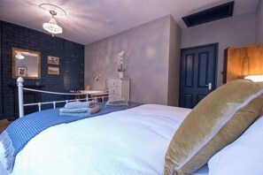 A bedroom with a large bed, a dresser, a mirror, and a chandelier.