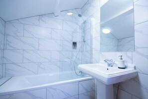 A modern bathroom with a glass-enclosed shower, white marble tiles, and a white sink with a mirror above it.