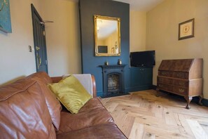 Ein Wohnzimmer mit braunem Ledersofa, Kamin, Fernseher und einem Holzkasten.