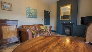 A room with a round wooden table, a brown leather sofa, a blue door, a fireplace, and a television.