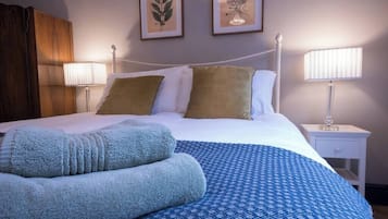A neatly made bed with a blue patterned bedspread, two pillows, and a folded blanket. There are two wall-mounted lamps on either side of the bed.