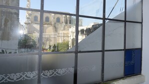 Blick durch ein Fenster mit Gittermuster, zeigt ein Gebäude mit Rundbogenfenstern und einem Kirchturm im Hintergrund.