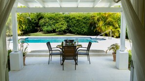 Une terrasse couverte avec une piscine, entourée d’une végétation luxuriante et de palmiers.