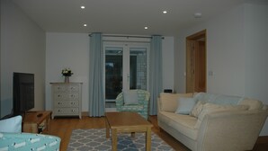 A living room with a sofa, a wooden coffee table, a patterned armchair, a TV, and a dresser. - Holiday Cottage 1 mile from Bruton (Bruton)