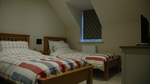 A bedroom with two single beds, a window with patterned curtains, a radiator, and a television on a stand. - Holiday Cottage 1 mile from Bruton (Bruton)