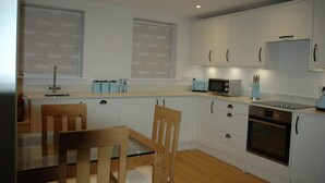 A modern kitchen with white cabinets, a microwave, an oven, and a dining area with a wooden table and chairs. - Holiday Cottage 1 mile from Bruton (Bruton)