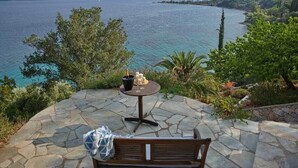A stone patio with a wooden bench and a small table, overlooking a body of water with distant land and trees. - Alonissos/Alonnisos - Idyllic Villa with private beach & jacuzzi,  amazing views (Alonissos)
