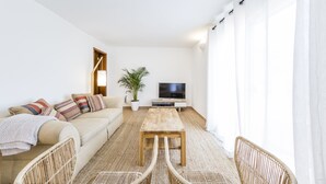 A modern living room with a sofa, a wooden coffee table, wicker chairs, a TV, and a potted plant. - Sea View !!! 2 bedrooms (Almancil)