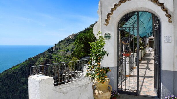 A coastal building with a wrought iron gate, a potted plant, and a view of the sea. - B&B NARCISO with private parking (Conca dei Marini, Campania)