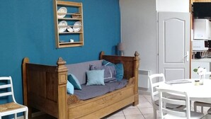 Una habitación acogedora con un sofá de madera, sillas blancas, una mesita pequeña y una repisa con vajilla.